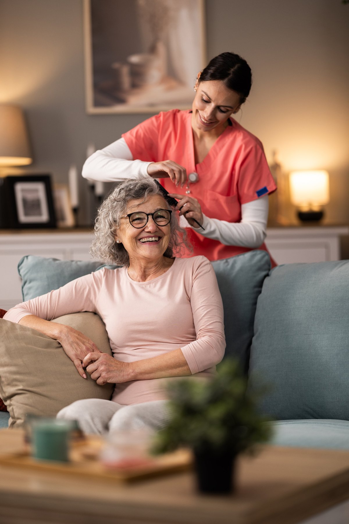 Young cheerful nurse combing senior woman's hair